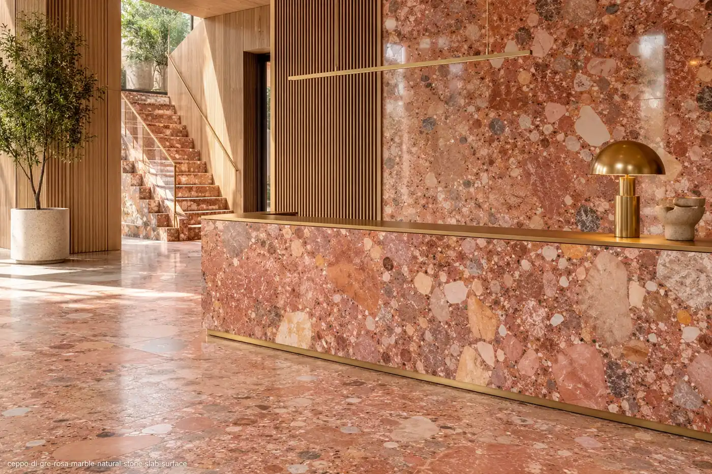 Warm conglomerate slab on a lobby counter, feature wall, staircase and flooring with coral, cream and blue-grey fragments.