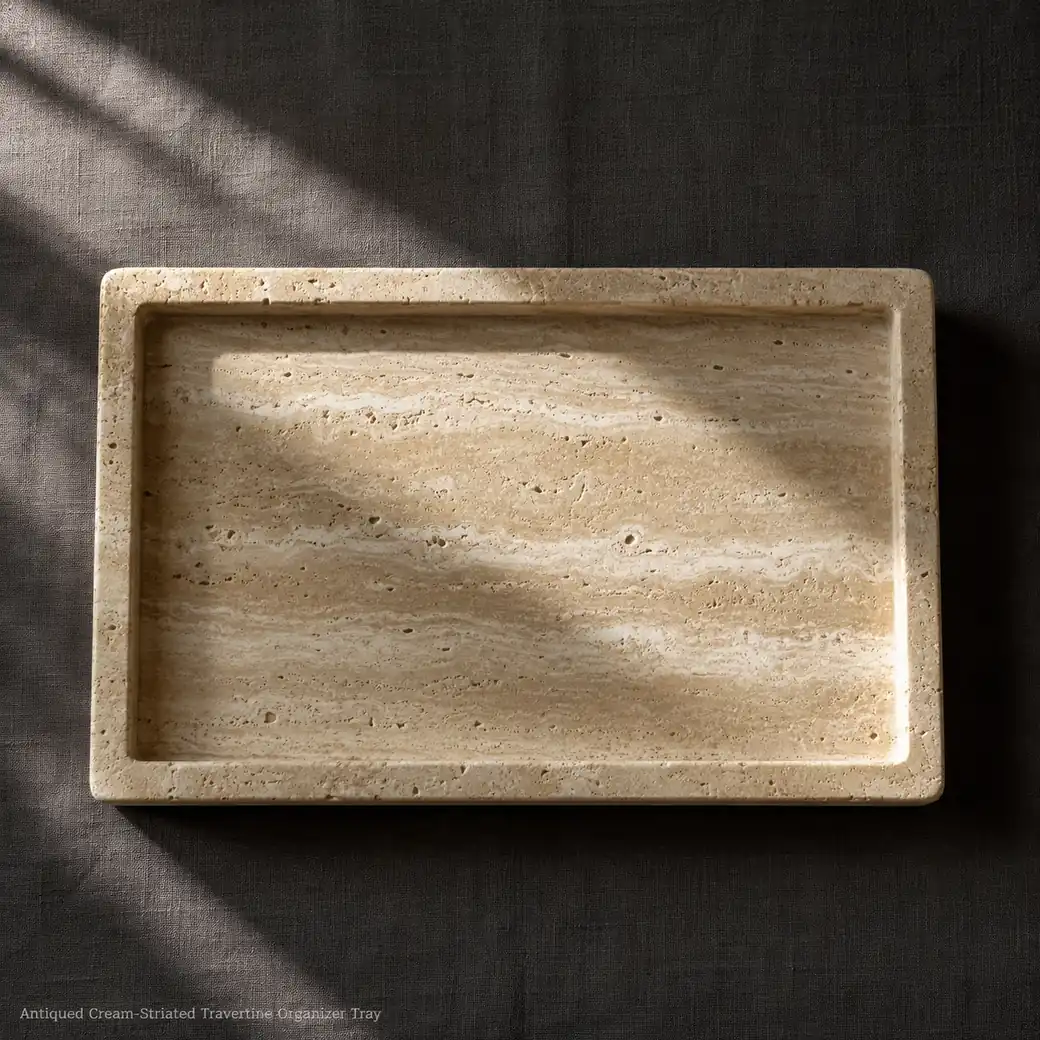 Antiqued travertine storage tray on charcoal linen, overhead view revealing cream striations and aged stone surface.