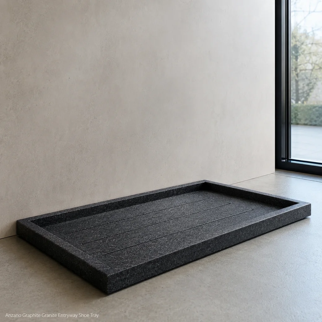Graphite granite shoe tray against pale entry wall, floor-level view showing drainage channels and textured 3 cm rim.