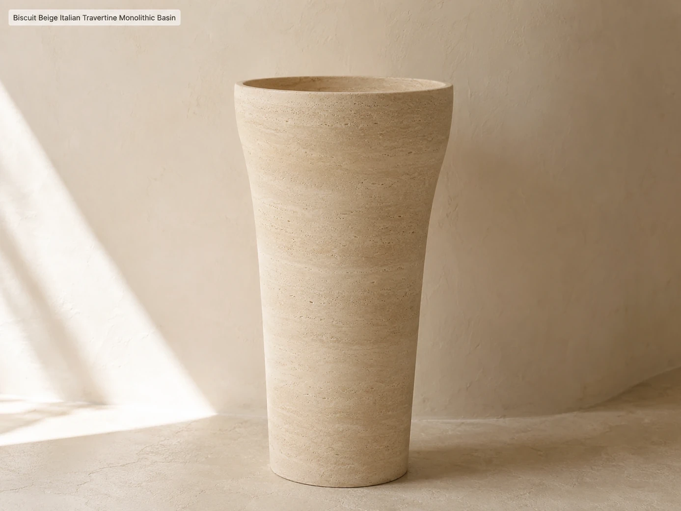 Biscuit beige monolithic travertine basin shown in right-side profile against a curved ivory wall