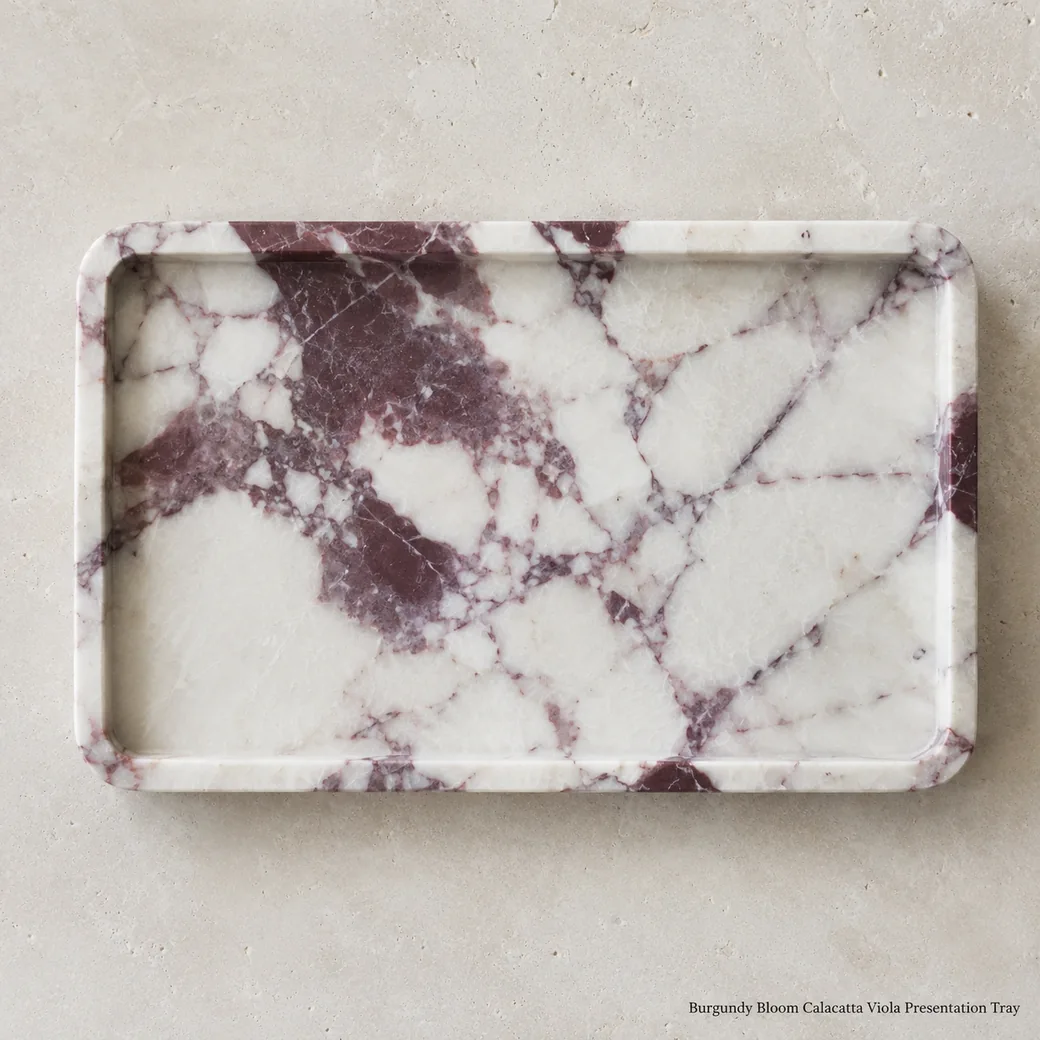 Overhead Calacatta Viola gift tray on pale limestone with plum-burgundy movement and brushed surface.
