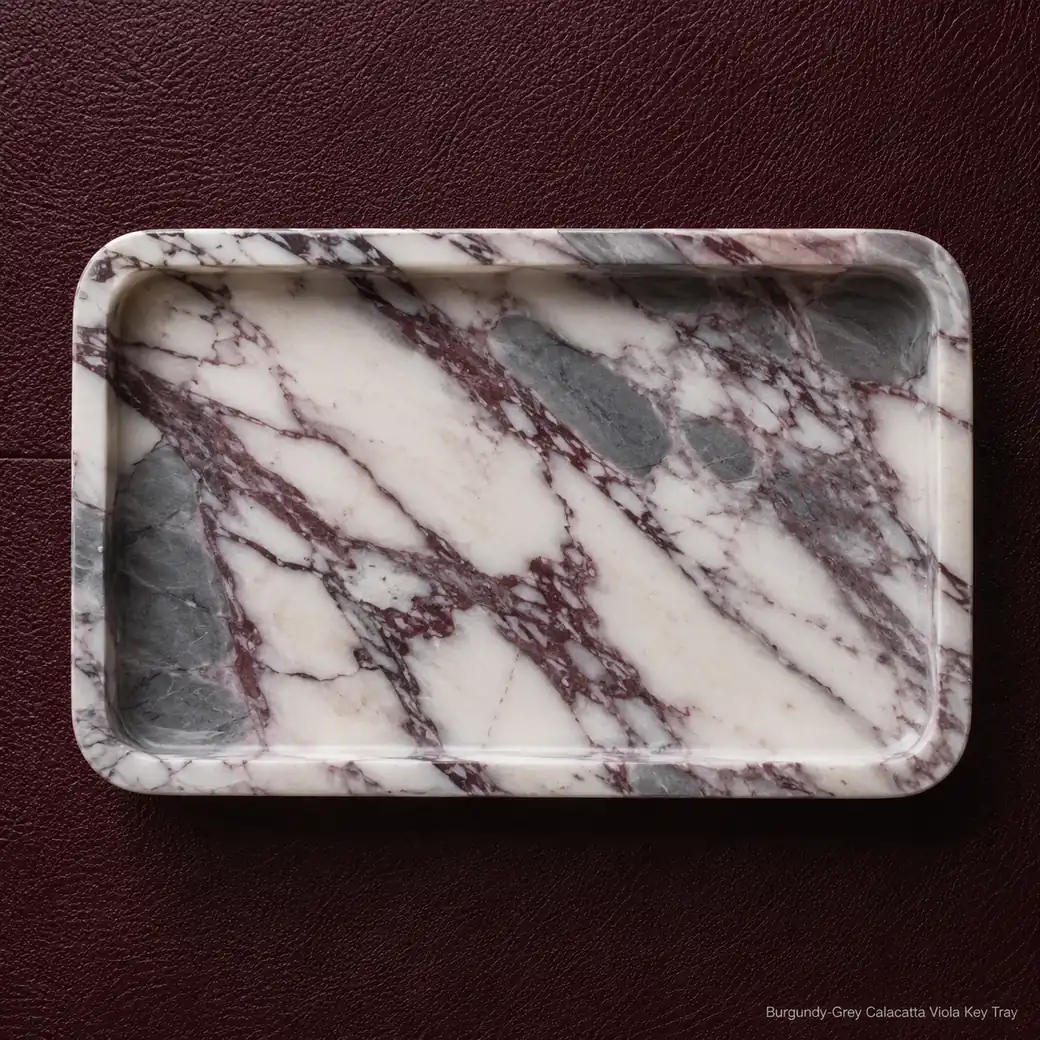 Calacatta Viola key tray on oxblood leather, overhead view showcasing burgundy-grey veining and brushed satin surface.