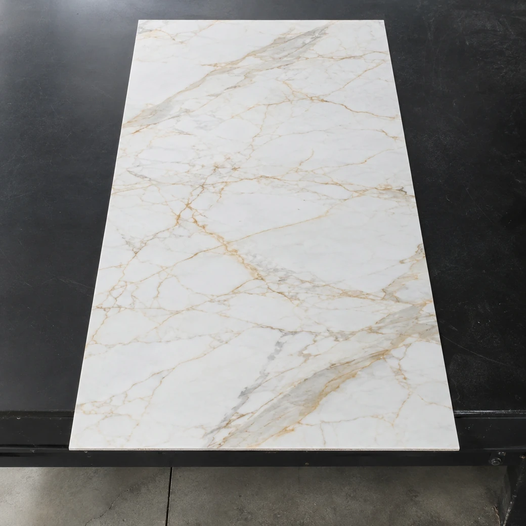 Overhead Calacatta Oro thin panel on black worktable with warm golden veining and visible 3 mm edge.