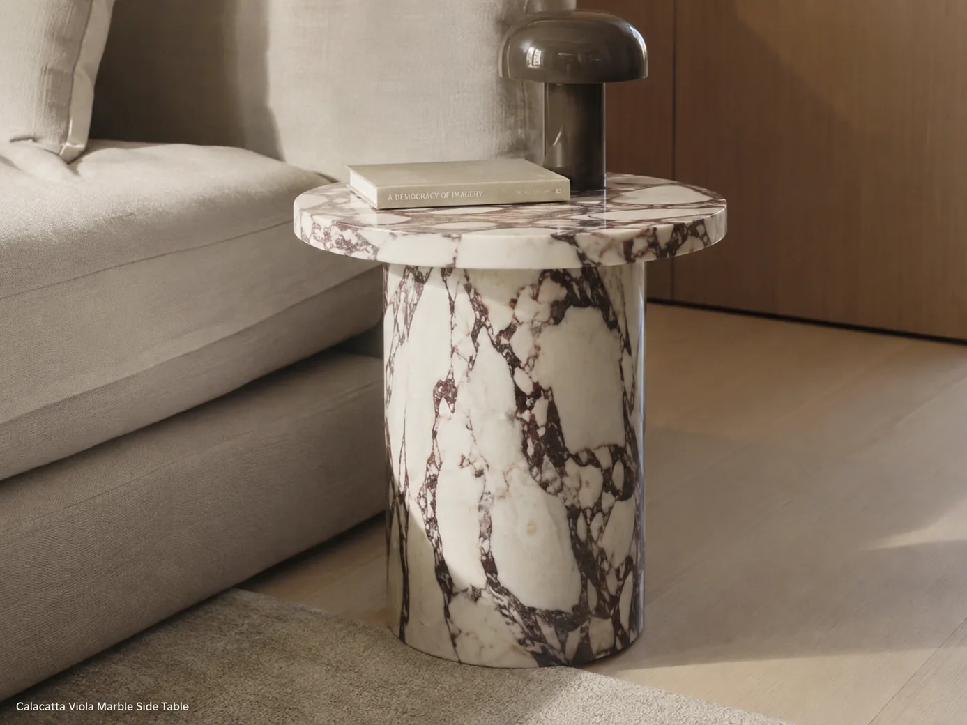 Polished Calacatta Viola side table beside a sofa with ivory stone, oxblood veining and sculptural pedestal