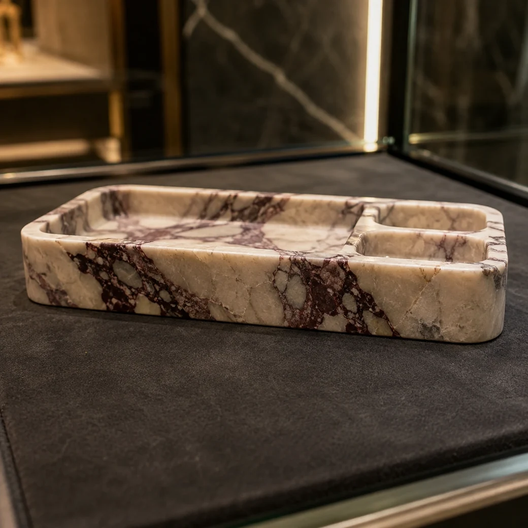 Low macro Calacatta Viola jewelry tray in a glass cabinet with burgundy-purple veins and carved sections.