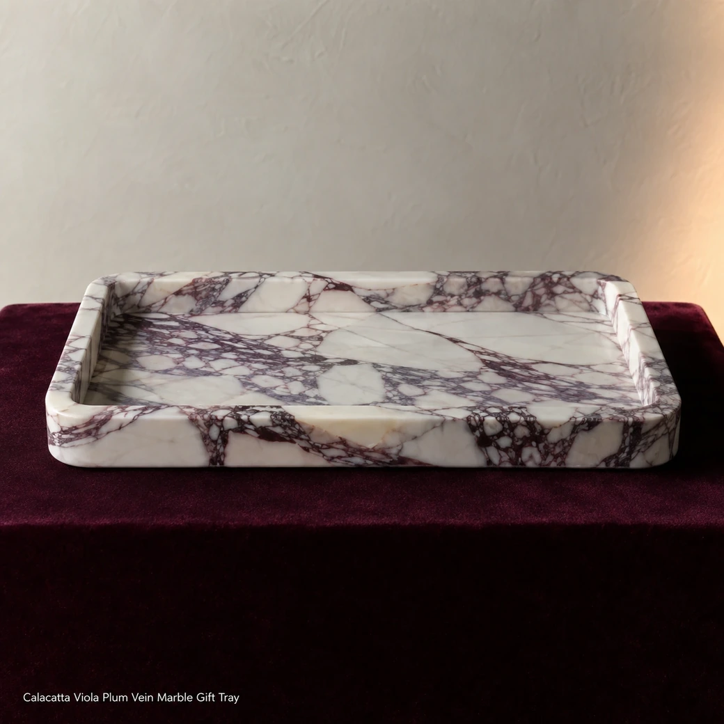 Calacatta Viola gift tray on burgundy velvet pedestal, low side view highlighting plum veining and brushed surface.
