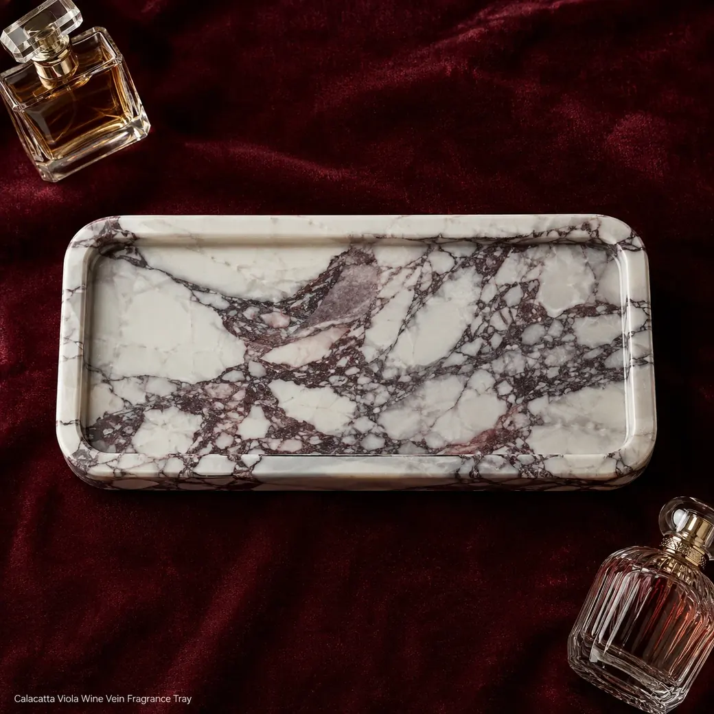 Overhead Calacatta Viola fragrance tray on burgundy velvet with dramatic marble movement across the centre.