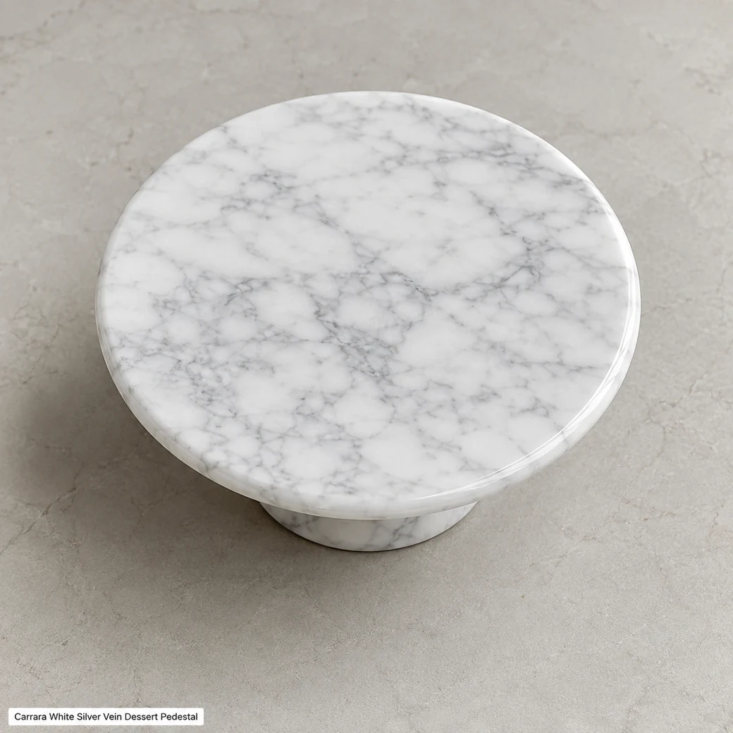 Top-biased Carrara cake pedestal on warm-grey stone, showing the polished circular surface, grey veining and base shadow.