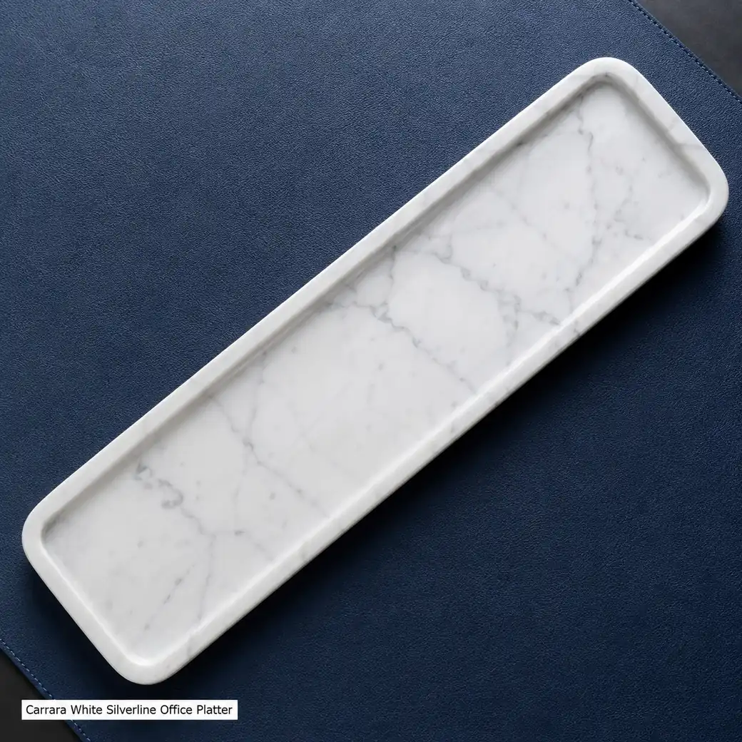 Overhead Carrara office tray on navy leather, displaying fine grey vein flow across its polished recessed surface.