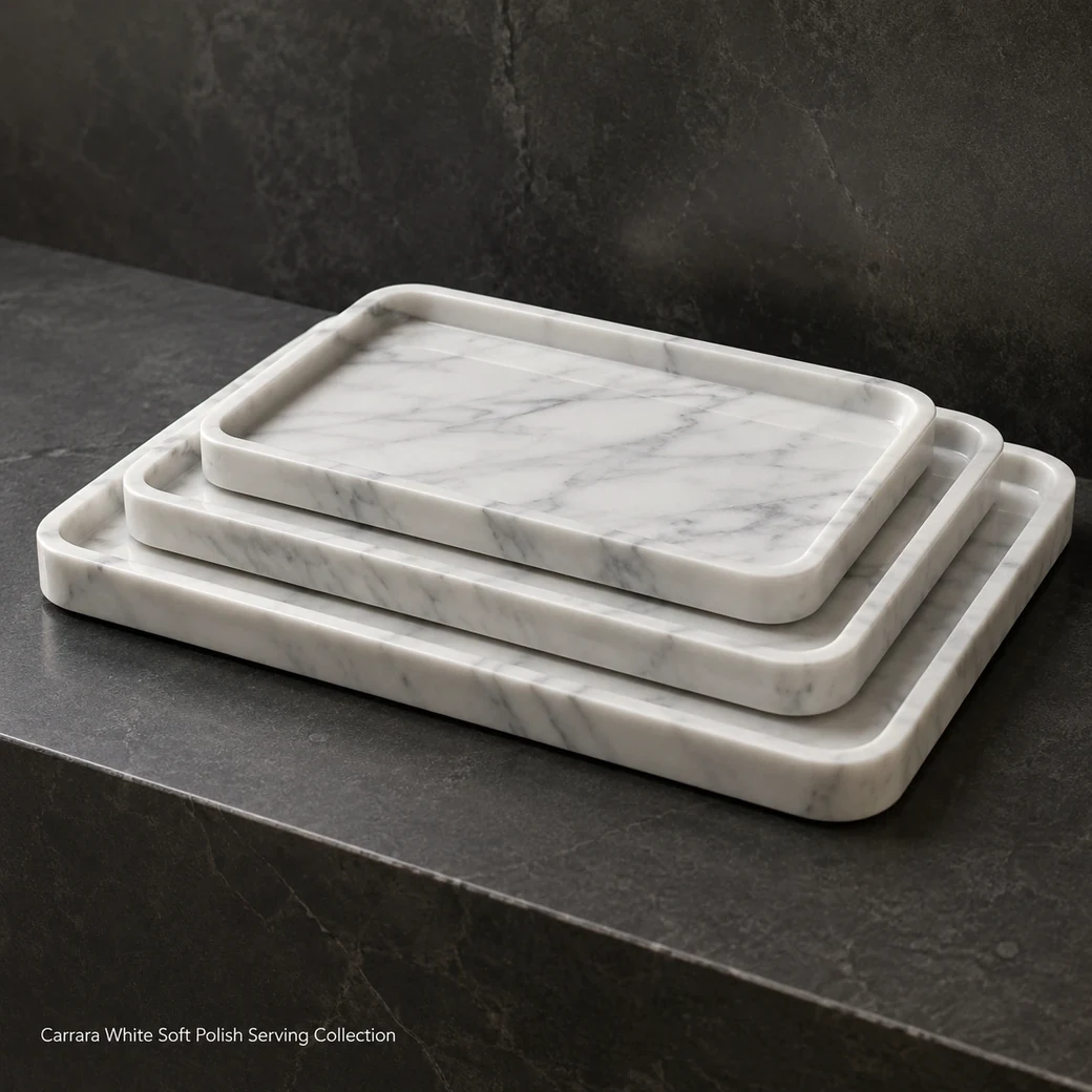 Carrara serving tray collection staggered on charcoal stone, low side view highlighting nested profiles and grey veins.
