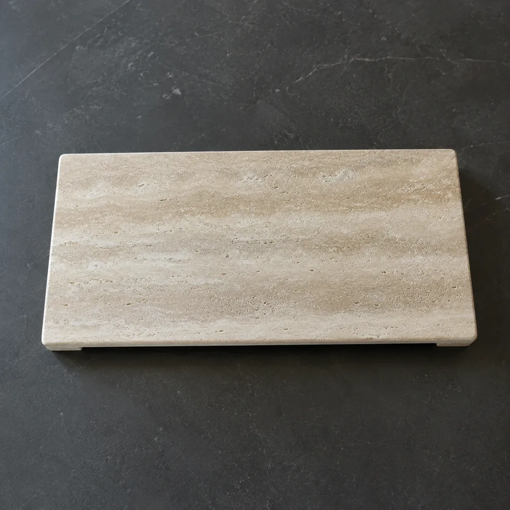 Overhead cream travertine accessory platform on charcoal, showing filled beige bands and slim shadow beneath the raised edge.