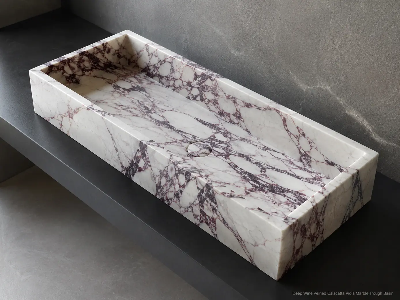 Top-down Calacatta Viola trough basin on graphite counter, revealing deep wine veins and the full linear bowl.