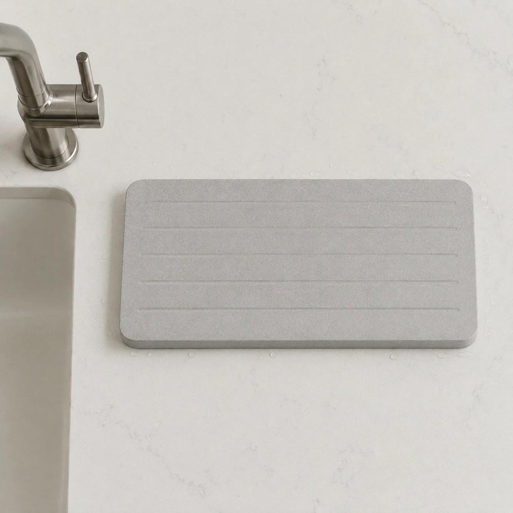 Overhead diatomite drain tray beside a steel faucet with light grey channels and porous matte texture.