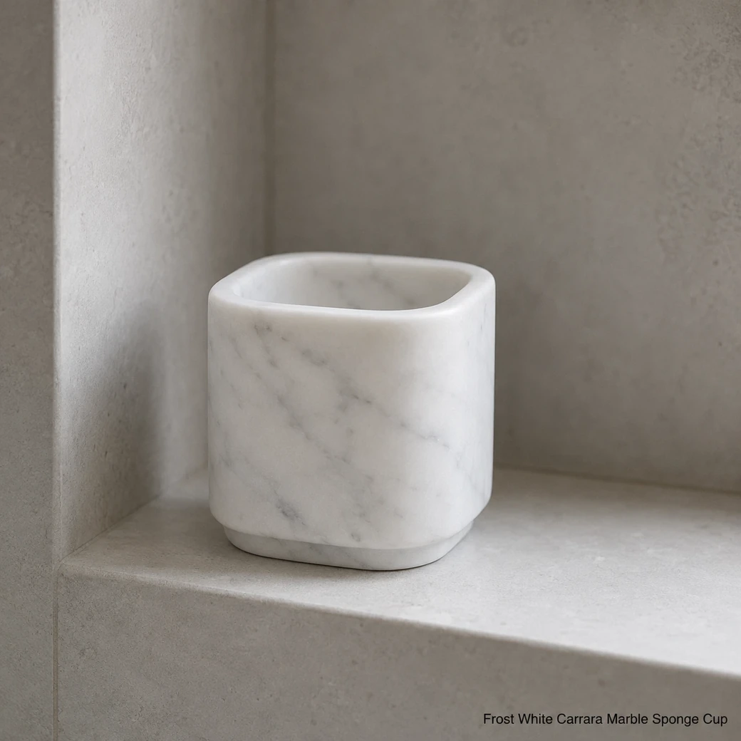 Frost white Carrara sponge cup in pale shower niche, low side view showing honed grey veining and drainage detail.