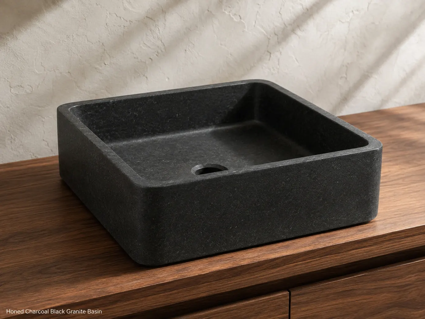 Charcoal black granite vessel basin viewed low on a walnut vanity against a pale plaster wall