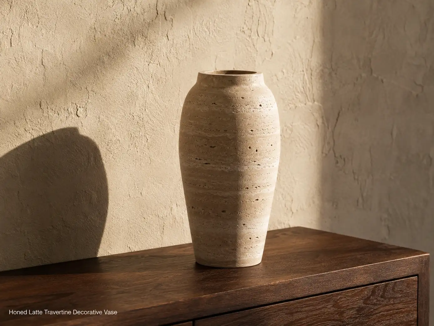 Latte travertine vase shown empty on dark walnut with warm side light and a sculptural shadow