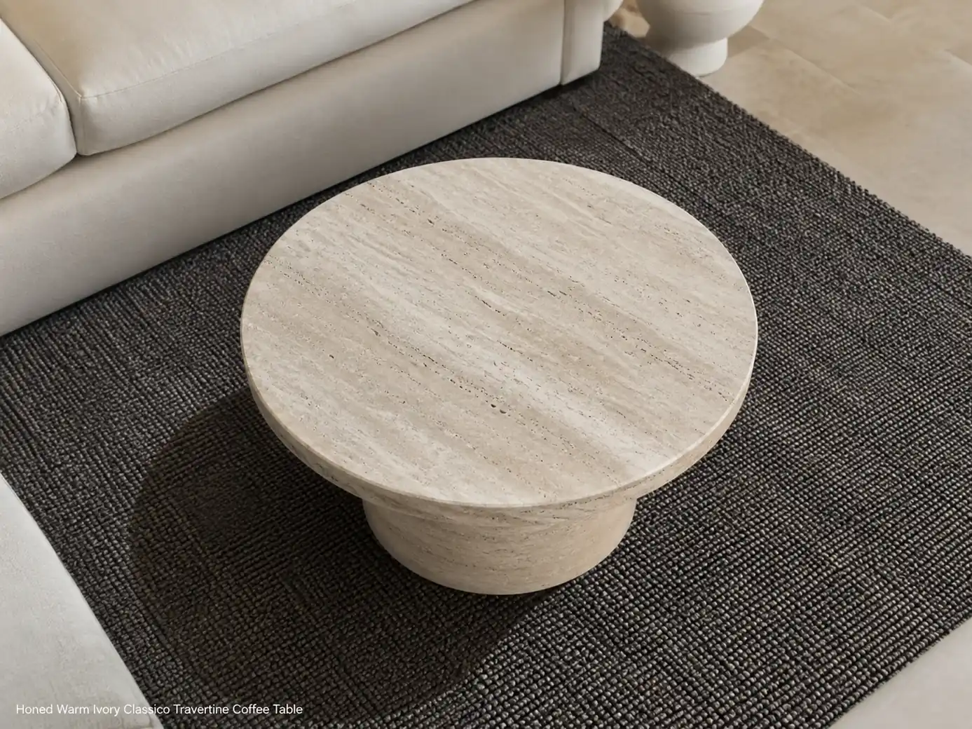 Warm ivory travertine coffee table viewed from above on a dark textured rug in a cream living room