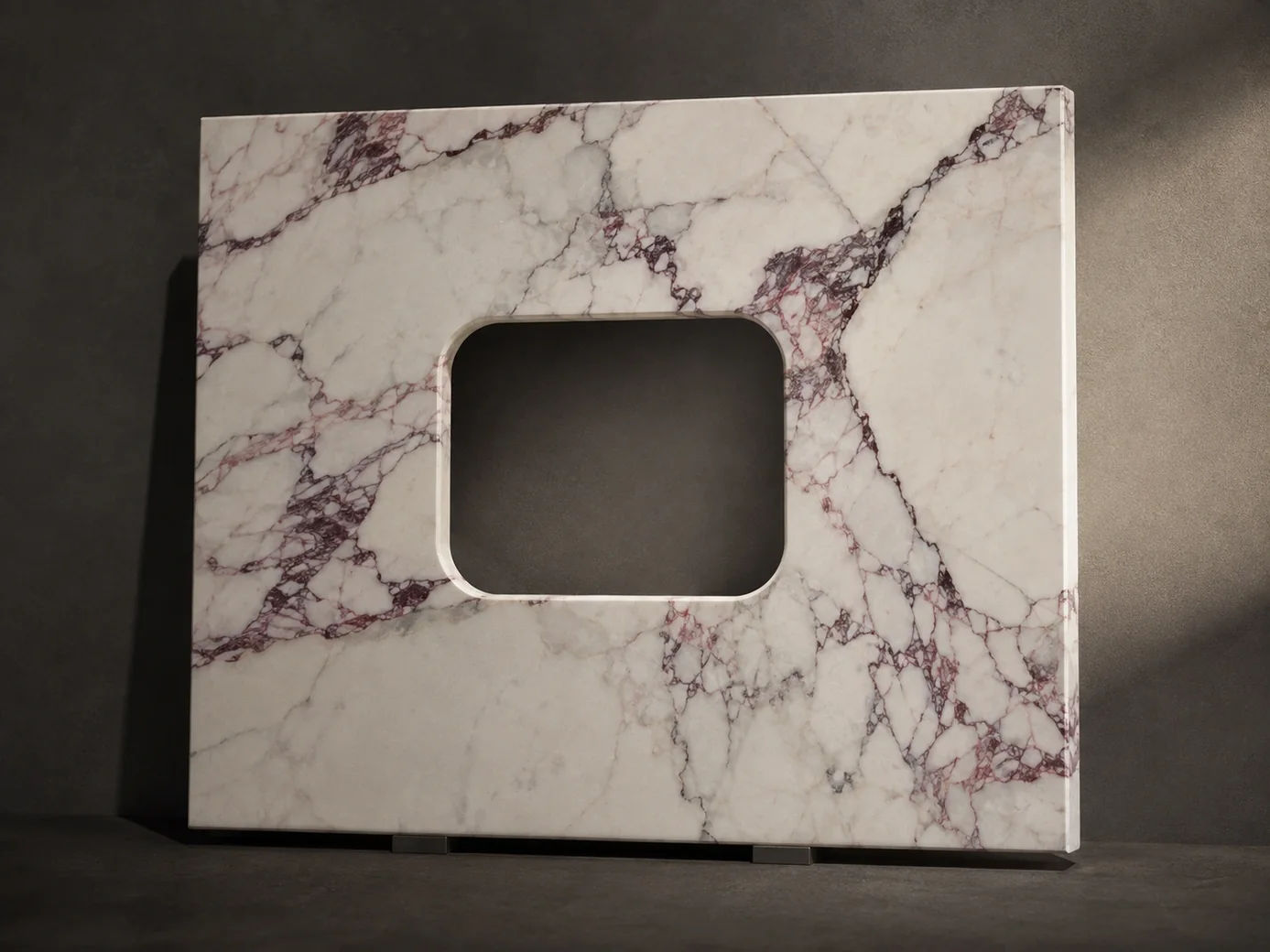 Wine-veined Calacatta vanity slab displayed upright against a dark gallery wall with raking light