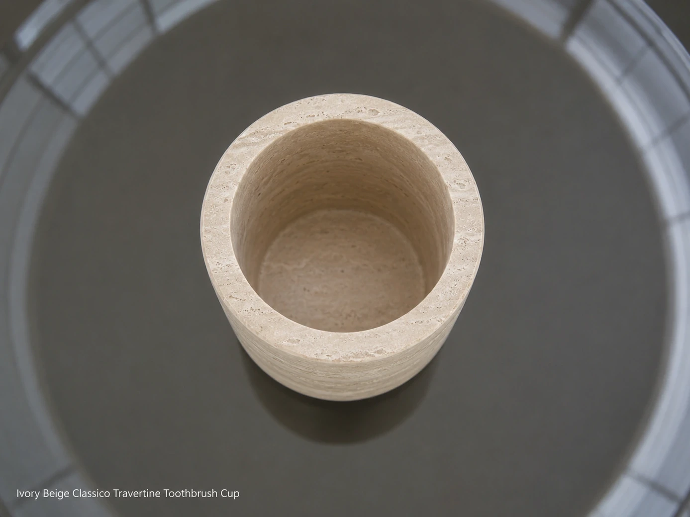 Ivory travertine toothbrush cup viewed directly from above on a dark smoked-glass vanity