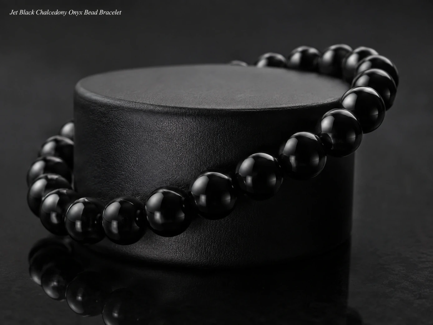Jet-black onyx bead bracelet draped around a matte-black display cylinder in a charcoal setting