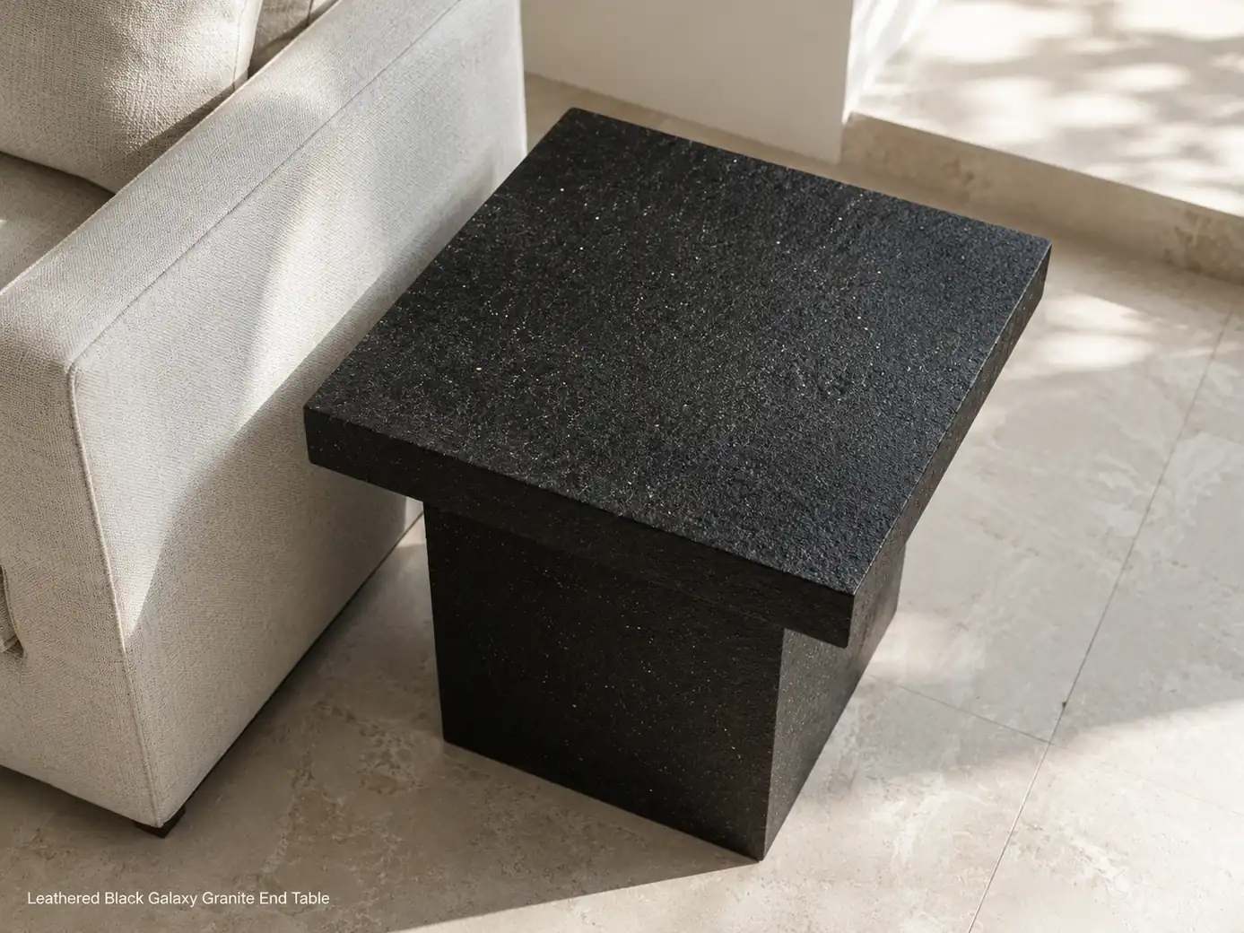 Leathered Black Galaxy end table beside a pale chair, viewed from above on a limestone floor