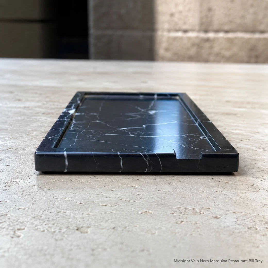 Nero Marquina bill tray on pale travertine, edge-level view emphasizing slim polished profile and white veins.