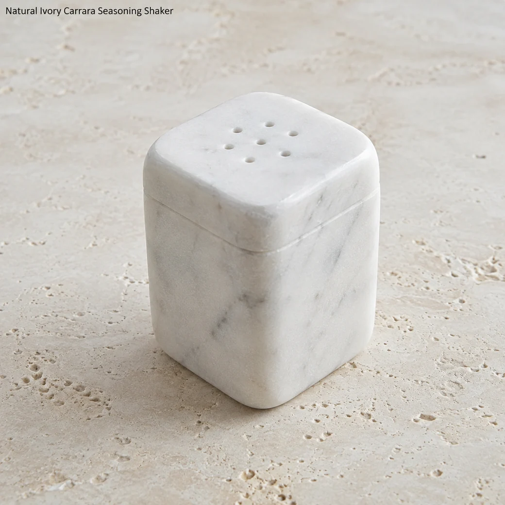 Ivory Carrara salt shaker on pale travertine, high rear view showing drilled top pattern and softened square form.