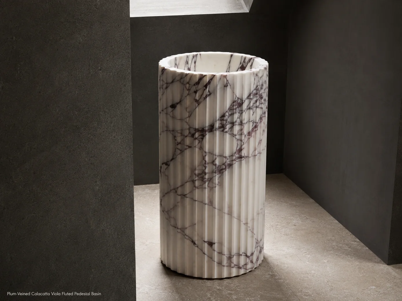 Plum-veined Calacatta Viola fluted basin viewed low from the rear in a dark architectural alcove