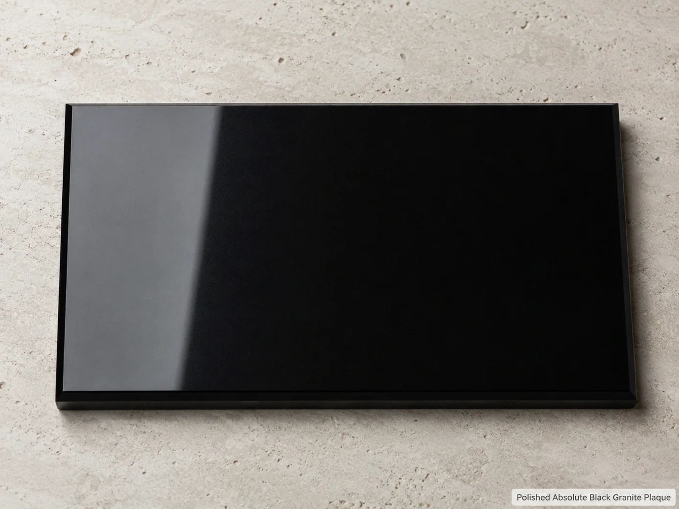 Blank mirror-polished black granite plaque lying flat on a pale limestone plinth, viewed overhead