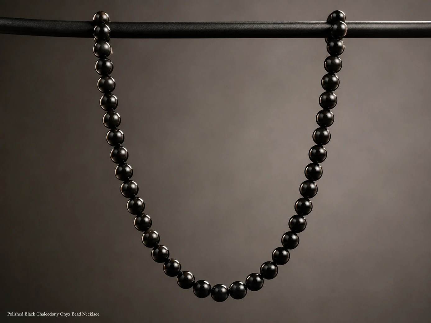 Black onyx bead necklace suspended from a display bar in a long U-shape with rim lighting