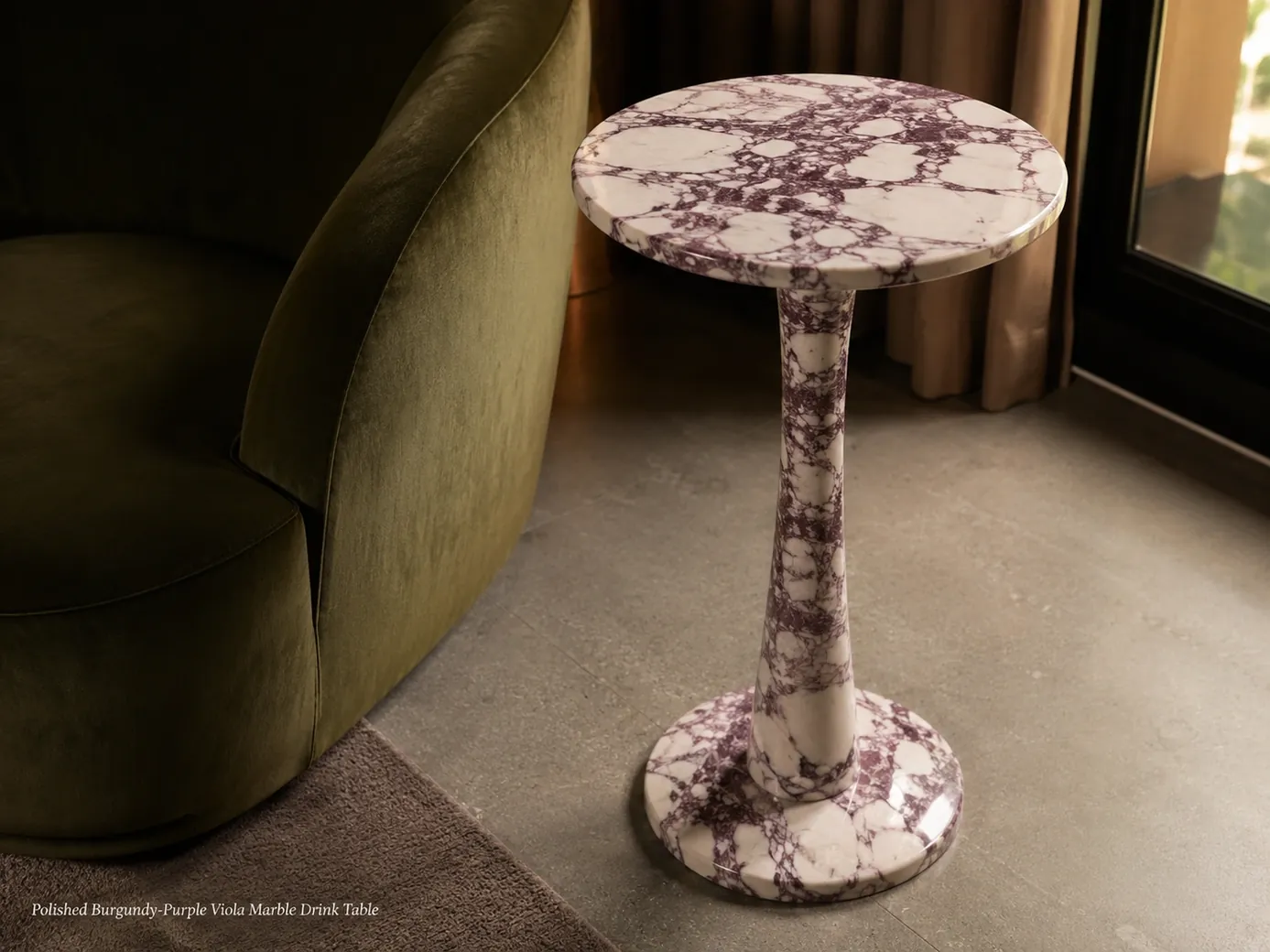 Polished burgundy-purple Viola drink table viewed from above beside a moss-green velvet chair