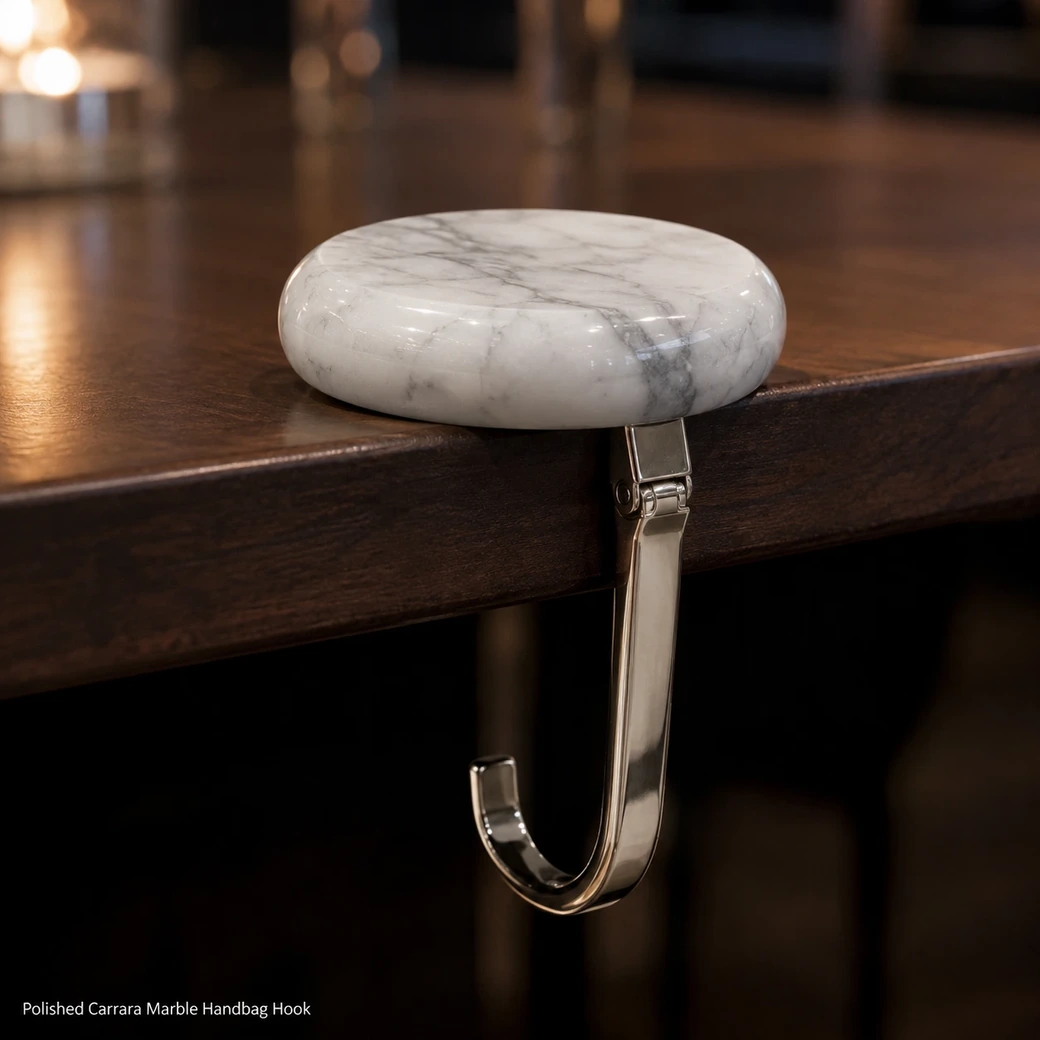 Polished Carrara handbag hook on restaurant table edge, close side view showing extended metal hook and marble top.