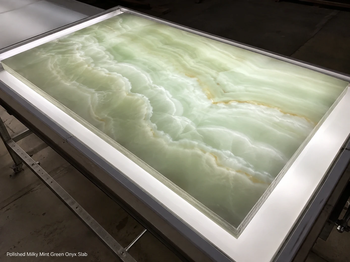 Mint green onyx slab laid on an illuminated inspection table and viewed from a high diagonal angle