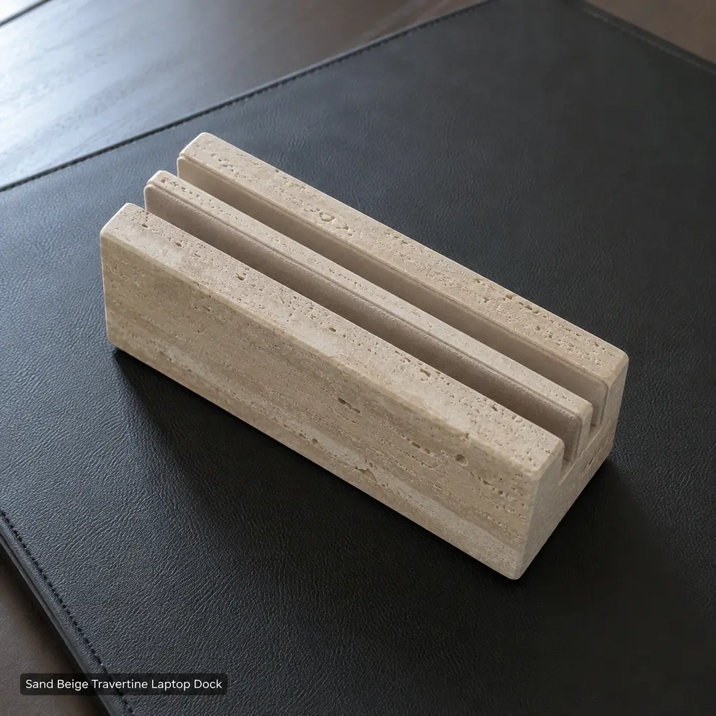 Sand beige travertine laptop dock on black leather pad, overhead diagonal view showing precision slots and honed pores.