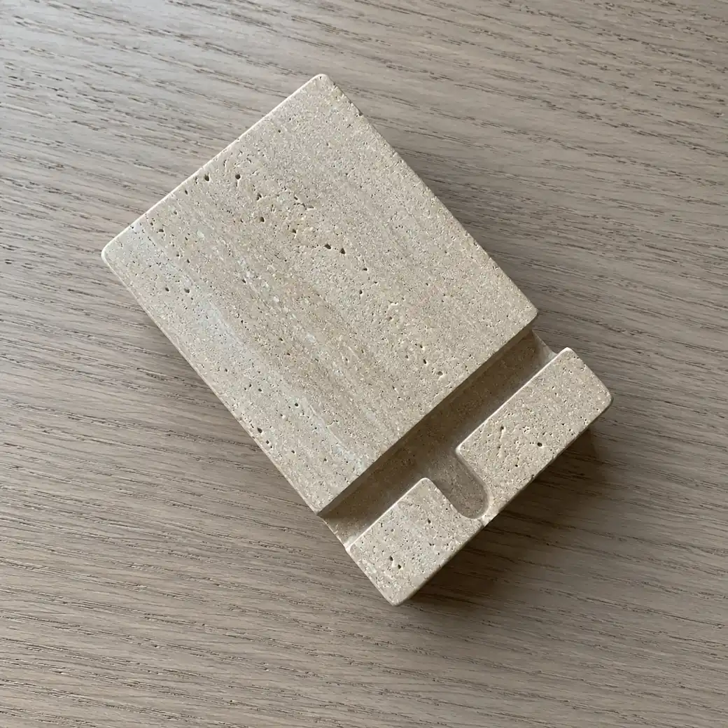 Overhead biscuit beige travertine phone dock on smoked oak with angled slot and satin-brushed pores.