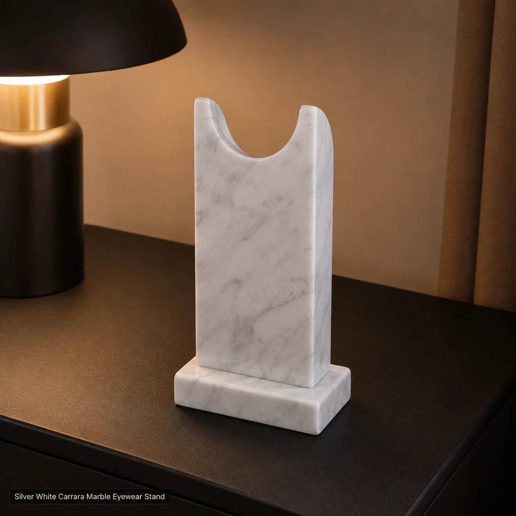 Silver white Carrara eyewear stand on dark bedside console, rear view showing curved cradle and polished grey veining.