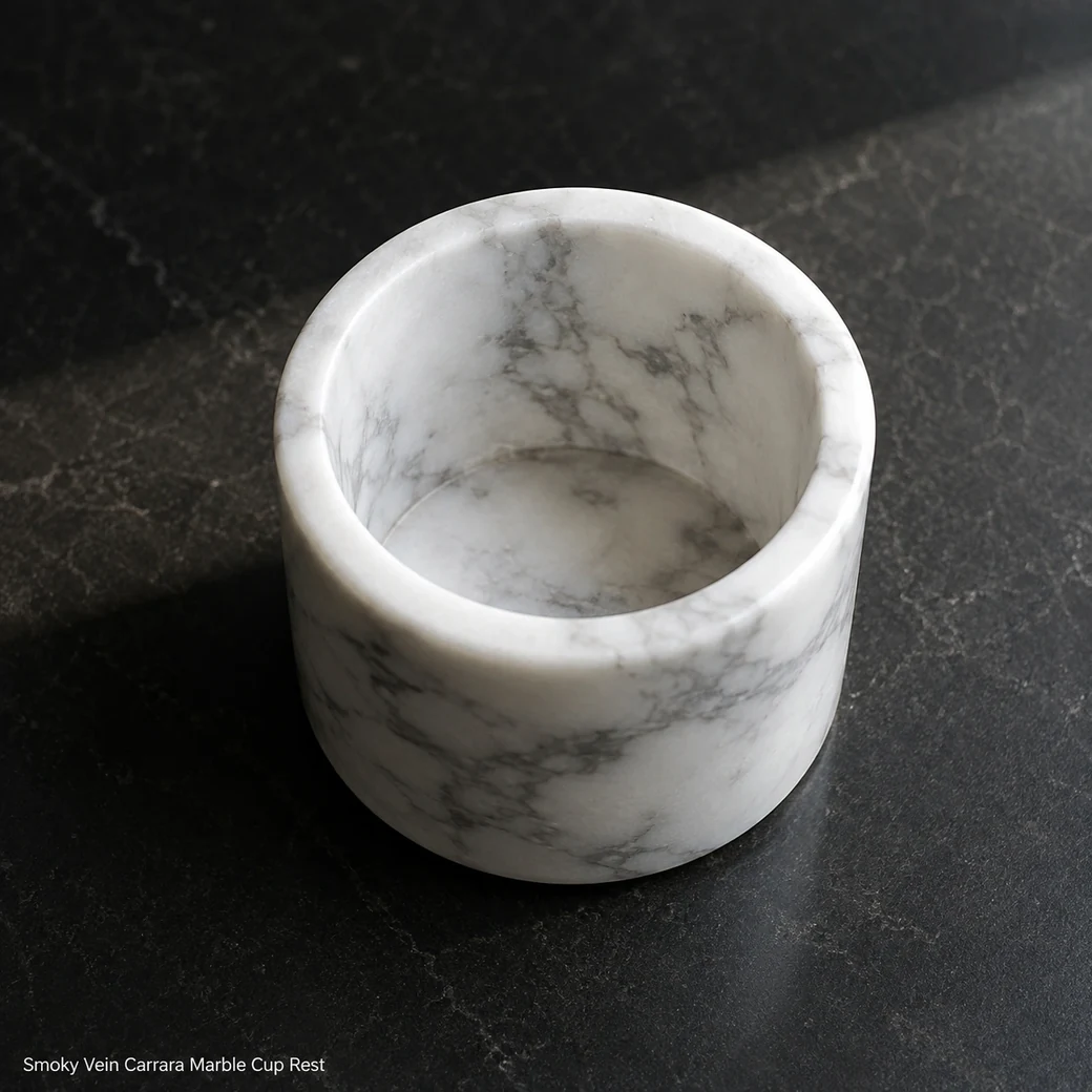 Carrara cup rest on black stone shelf, overhead diagonal view showing smoky grey veins and smooth inner cavity.