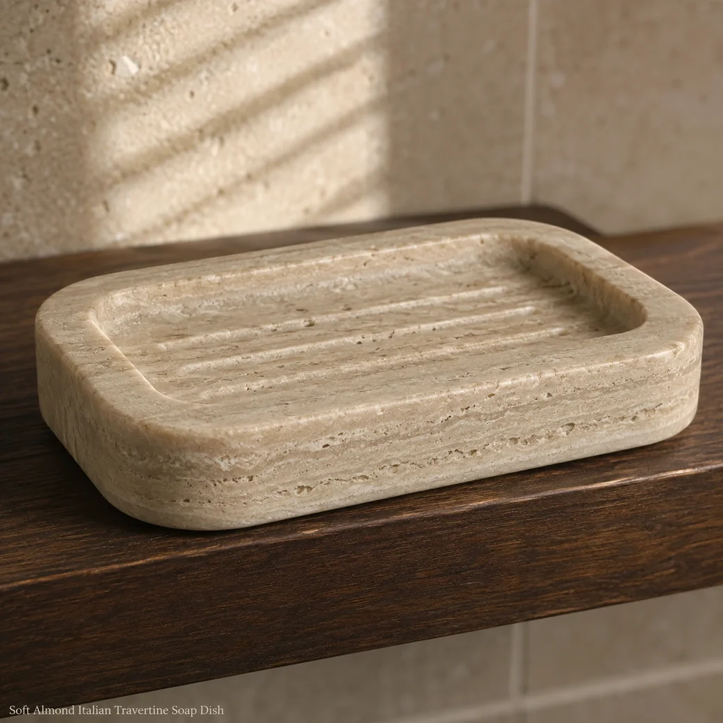 Soft almond travertine soap dish on dark walnut shelf, macro low view showing satin finish and drainage grooves.