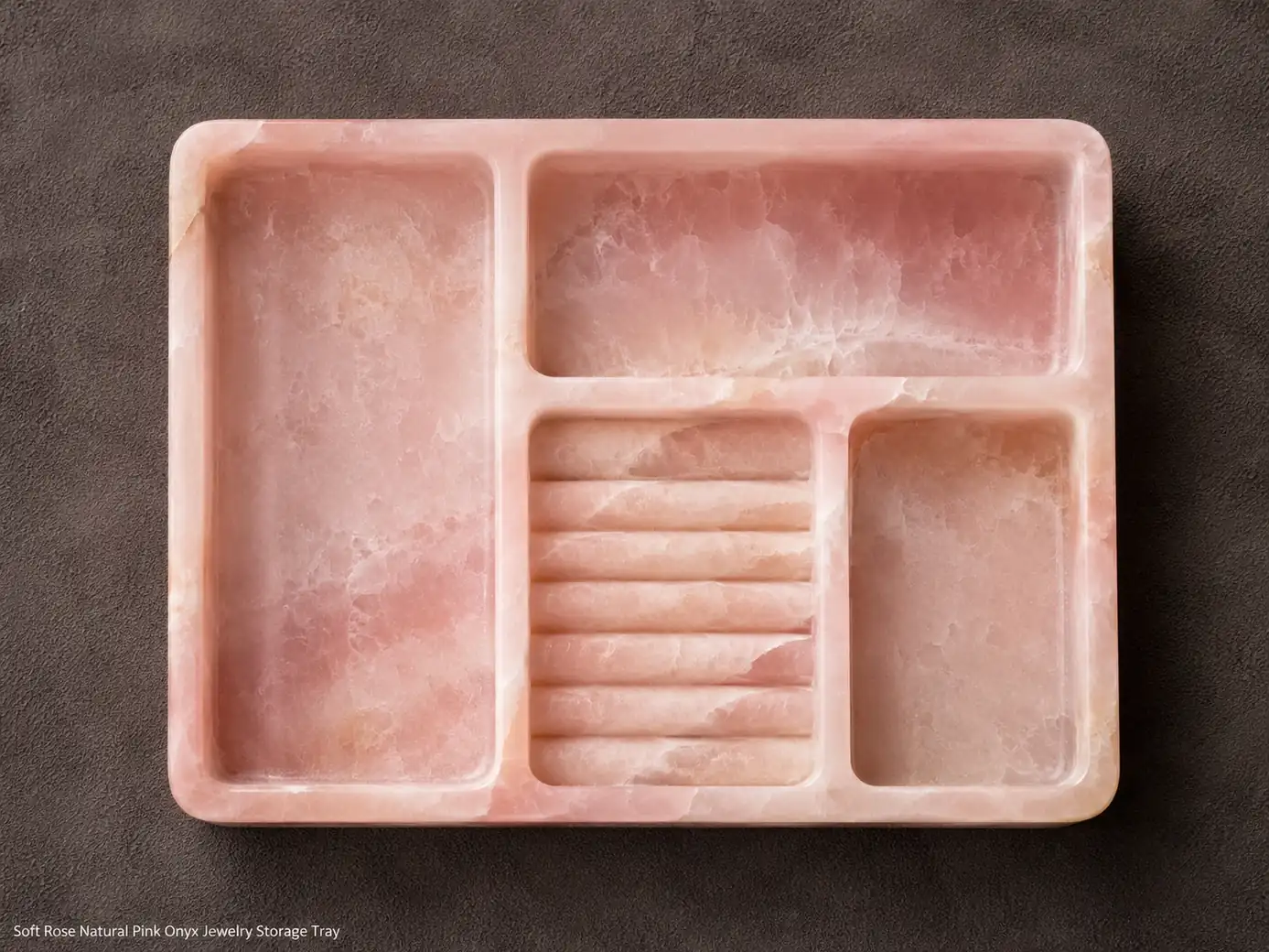 Top-down Natural Pink Onyx jewelry tray on grey suede, revealing carved compartments and soft rose mineral detail.
