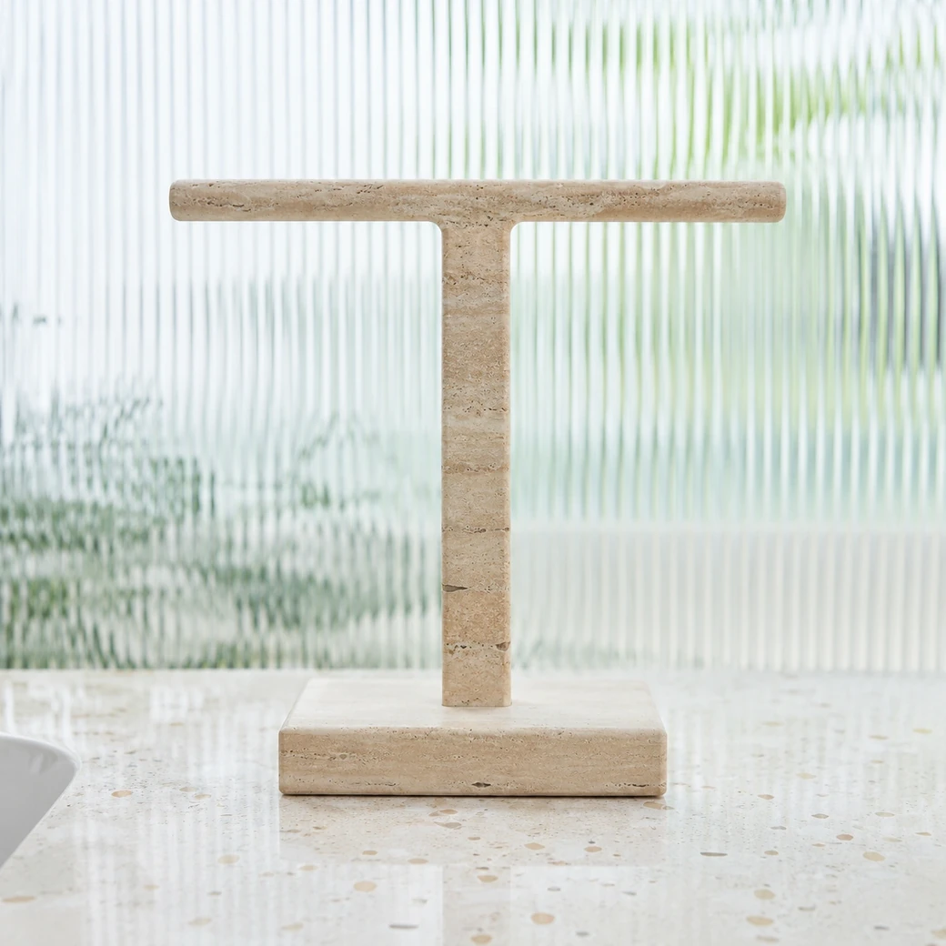 Front-view creamy tan travertine towel stand on terrazzo with sculptural profile and sanded-honed bands.
