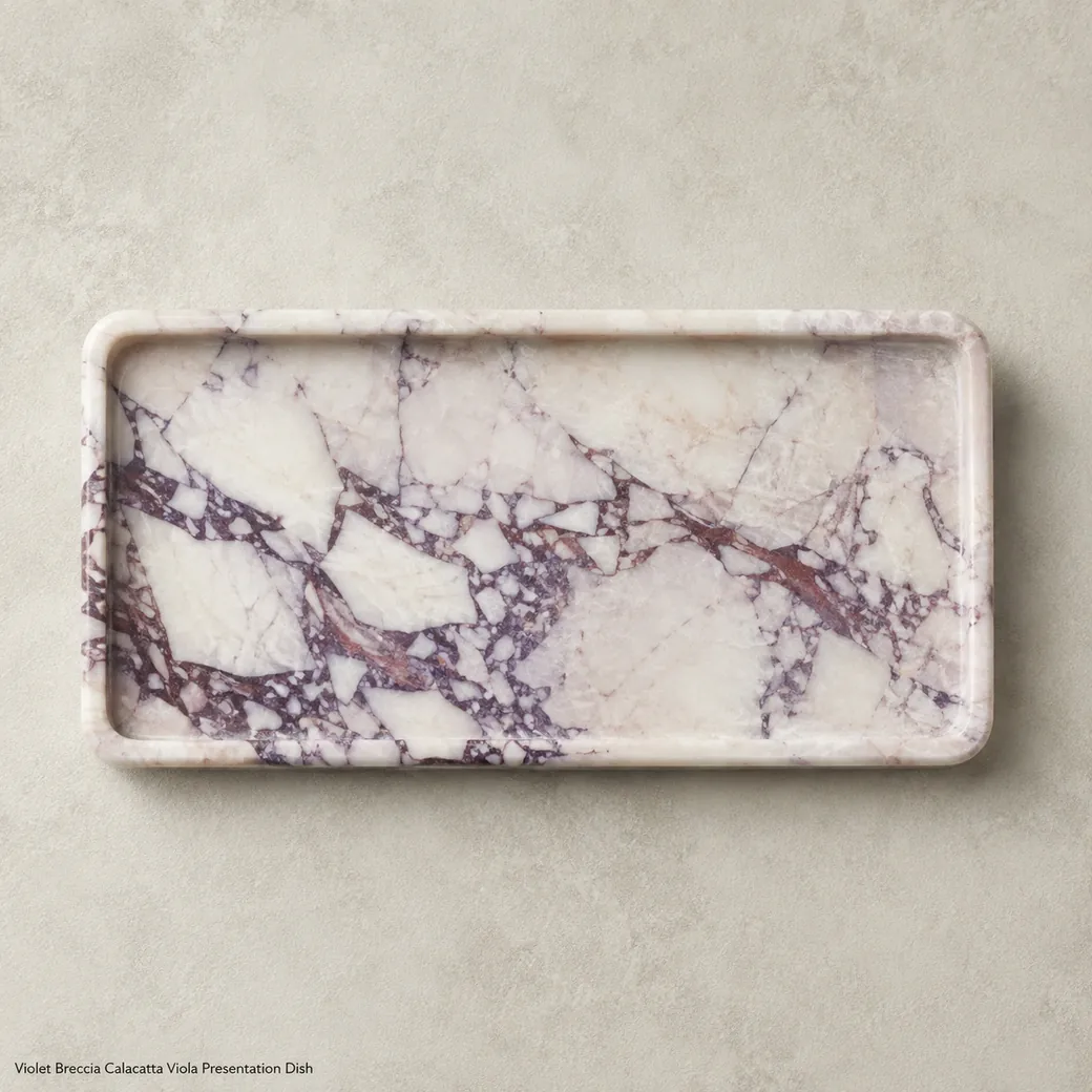 Overhead Calacatta Viola display tray on ivory suede with purple-red veins and fine-brushed texture.