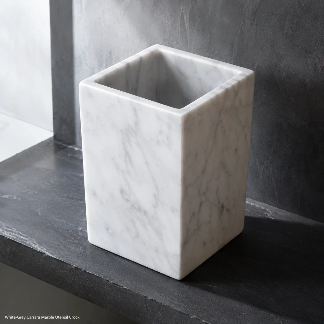 White-grey Carrara utensil crock on dark basalt shelf, elevated rear view showing deep cavity and matte veined surface.